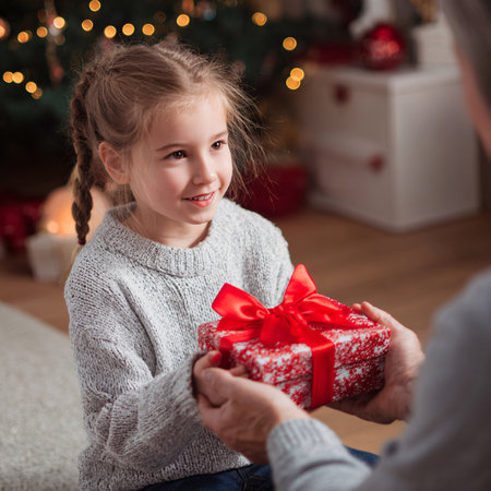 A young Caucasian girl with braided hair receives a gift from an adult in a cozy, decorated room.の素材