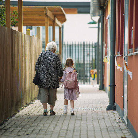 An elderly woman and a young girl walk hand in hand down a paved path in a residential area.の素材