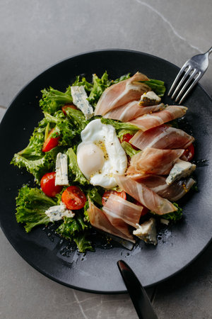 Delicious salad - jamon, cheese, egg and fresh vegetables on a gray background. Salad in a restaurant. Health food. close-up.の写真素材