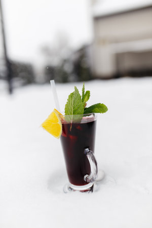 Mulled wine in the snow. Mulled wine in a glass mug, hot red wine with orange and apple, spices with cinnamon, pouring into a glass. Beautiful white background. copyspace.の写真素材