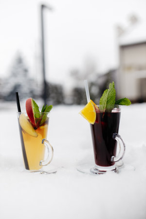 Mulled wine in the snow. Mulled wine in a glass mug, hot red wine with orange and apple, spices with cinnamon, pouring into a glass. Beautiful white background. copyspace.の写真素材