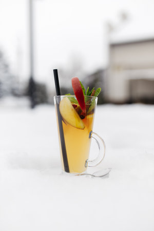 Mulled wine in the snow. Mulled wine in a glass mug, hot red wine with orange and apple, spices with cinnamon, pouring into a glass. Beautiful white background. copyspace.の写真素材