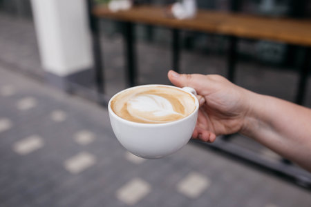 Woman holding latte art coffee on wooden table in coffee shop. Coffee in a mug.の写真素材