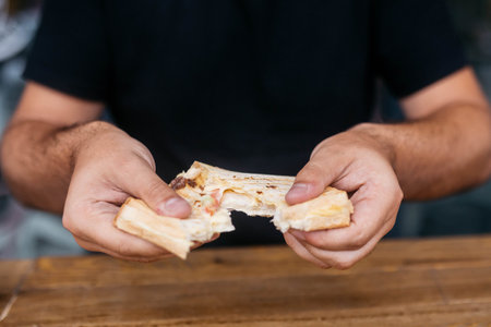 The guy holds a piece of sandwich in his hands and tears it. Sandwich in the hands of a guy.