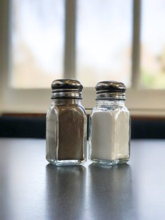 Salt and pepper pots stand next to each other on the table.の写真素材