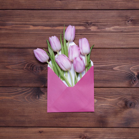 Pink tulip flowers in envelope on brown wooden backgroundの写真素材