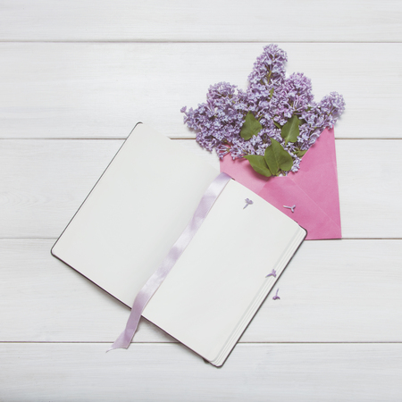 Clean sheets notepad with lilac flowers bouquet in envelope on white wooden backgroundの写真素材