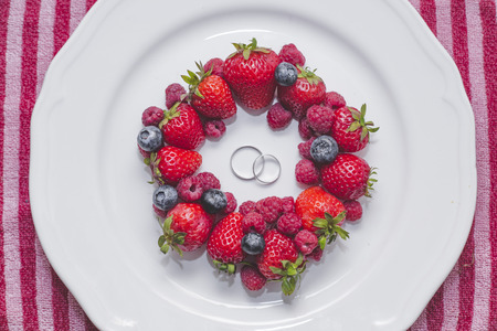 Wedding rings on plate with fresh berriesの写真素材