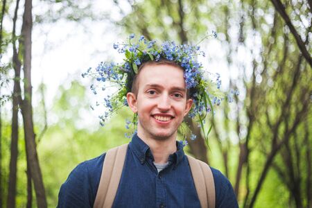 Handsome man with a wreath of blue forget-me-nots flowers on his headの写真素材