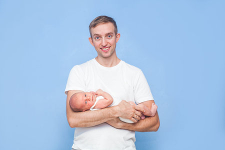 Newborn baby in father's arms on blue wall background