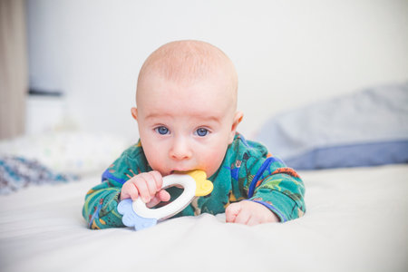 Three month baby boy lies on stomach and puts a toy in his mouthの写真素材