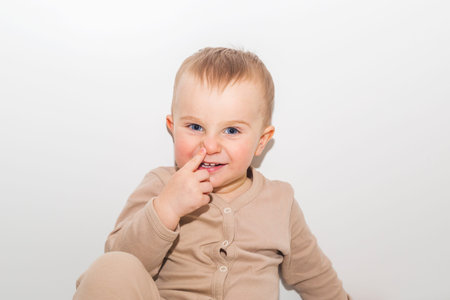 Little boy points to his nose on white wall background