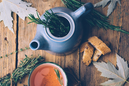 Rosemary and thyme herbal fall tea. Old wooden background with teapot, cup, herbs and leaves. Relax and peaceful mood.の写真素材