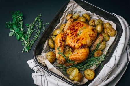 Roasted chicken with thyme served on black baking dish with potatoes, oranges and spices on wooden table. Thanksgiving or Christmas dinner. Top viewの写真素材