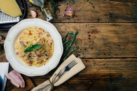 Spaghetti Carbonara. Pasta alla carbonara with a cream sauce, bacon and pepper on a white plate. Old wooden background. Copy space.の写真素材