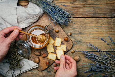 Honey in a jar with wooden honey dipper on a wooden board with crackers, nuts and lavender flowers. Copy spaceの写真素材