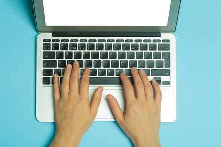 Female hands behind a laptop. Female hands work on a computer keyboard on the Internet on a blue background of the workplace.の写真素材