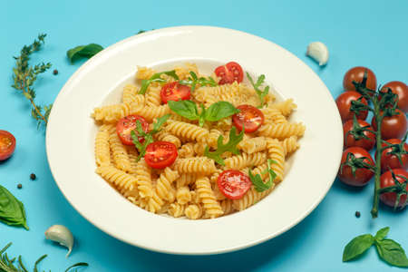 Food pasta on a blue background. Italian fusilli pasta with tomatoes, herbs and basil on a white plate. Healthy food concept.の写真素材
