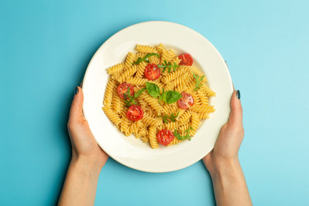Pasta food on a blue background with female hands. Italian fusilli pasta with tomatoes and basil on...