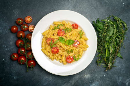 Food pasta on a dark background. Italian fusilli pasta with tomatoes, herbs and basil on a white plate. Healthy food concept.の写真素材