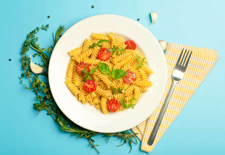 Food pasta on a blue background. Italian fusilli pasta with tomatoes, herbs and basil on a white plate. Healthy food concept.の写真素材