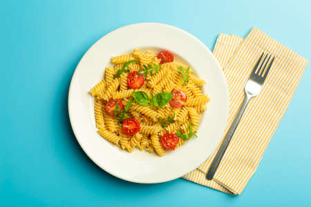 Food pasta on a blue background. Italian fusilli pasta with tomatoes, herbs and basil on a white plate. Healthy food concept.の写真素材