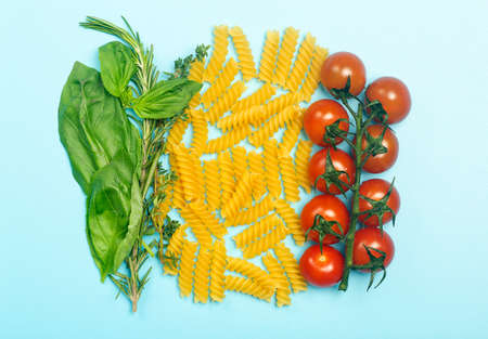 Raw fusilli pasta with tomatoes, herbs and basil. Italian pasta with ingredients in the colors of the Italian flag.の写真素材