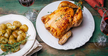 Roasted chicken with thyme served on white plate with potatoes, oranges and spices on wooden table. Thanksgiving or Christmas dinner. Top viewの写真素材