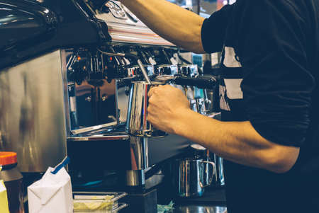 Coffee barista at work. Making cappuccino or latte on a coffee machine in an outdoor coffee shop.の写真素材