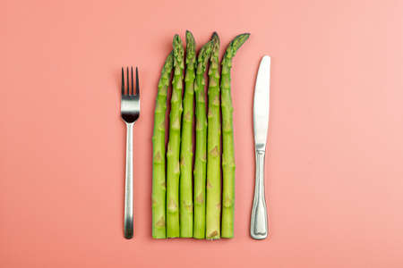 Asparagus with fork and knife on a pink background. Fresh vegetable asparagus for a healthy diet and nutrition. Vegetables and healthy food conceptの写真素材