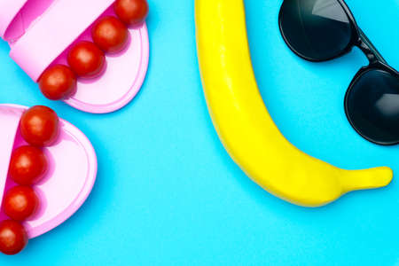 Creative summer minimal background with sunglasses, plastic banana and sandals. Flat lay concept in bright pastel colorsの写真素材