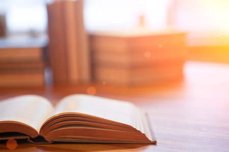 Book background. Blurred open book on a table in a university or school library in the sunlight from...