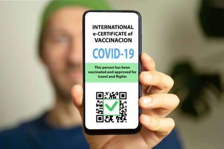 The men is holding a smartphone with electronic coronavirus vaccination certificate or vaccine passport for travellers. COVID-19 immunity e-passport mobile app for international travellingの写真素材