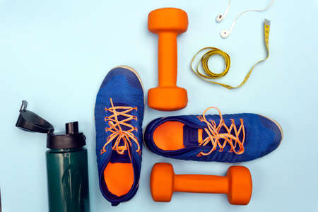 Sport concept with sport equipment composition. Sneakers, dumbbells, bottle of water on bright blue backgroundの写真素材