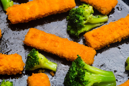 Fish sticks background. Fried fish sticks and baked broccoli on a cooking tray as an appetizer and food for children and parties.の写真素材