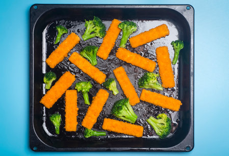 Fish sticks background. Fried fish sticks and baked broccoli on a cooking tray as an appetizer and food for children and parties.の写真素材