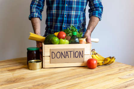 Food donation concept. A man holding a donation box with vegetables, fruits and other food for donationの写真素材