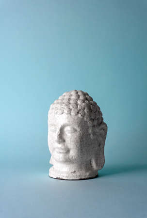 Ceramic head of a Buddha on a blue background. Minimal concept, copy spaceの写真素材