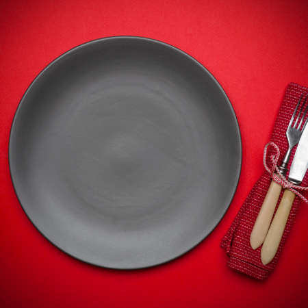 Empty plate on a red background table with a knife and fork. Festive tableware for a festive dinnerの写真素材