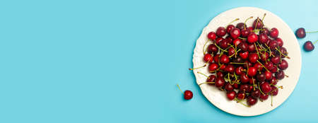 Cherry banner background. Red juicy sweet cherry on a white plate on a light blue background. Summer fresh juicy berries and food concept. high quality photoの写真素材