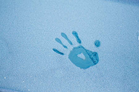 Palm trail on the frozen glass of a car covered with hoarfrost.の写真素材