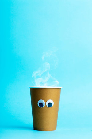 A paper cup with hot coffee and eyes on a blue background. Funny food concept.