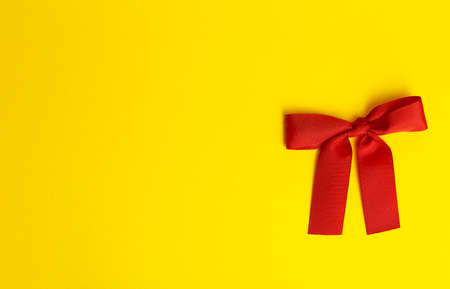 Gift bow on a yellow background. Red gift bow with shadow on a colored yellow background. Gift concept. Minimal copy spaceの写真素材