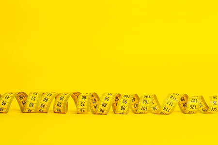 Measuring tape on a yellow background. Measuring tape in the shape of a spiral twisted on a yellow background. Slimming and diet concept, copy space.の写真素材