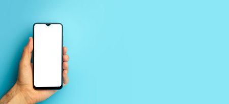 Empty smartphone in hand on colored blue banner background. Mockup phone with blank screen on...
