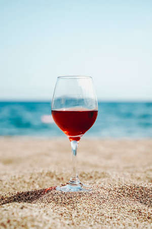Glass of red wine against the background of the Mediterranean beach and the sea in a tourist town in the summer under sunlight. Summer, travel, lifestyle, relaxation, and enjoyment concept. high quality photoの写真素材