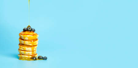 Pancakes with berries on a blue banner background. Lush delicious pancakes with blueberries and syrup for brunch on a minimal colored background. Beautiful bright food photo. high quality photoの写真素材