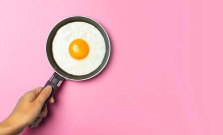 Fried egg is minimal. Fried egg in a frying pan on an empty pink background. Creative breakfast and food idea.の写真素材