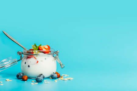 Yogurt with granola, fresh berries and nuts in a jar on a blue background. Healthy breakfast and dessert milk concept. Beautiful bright food photoの写真素材