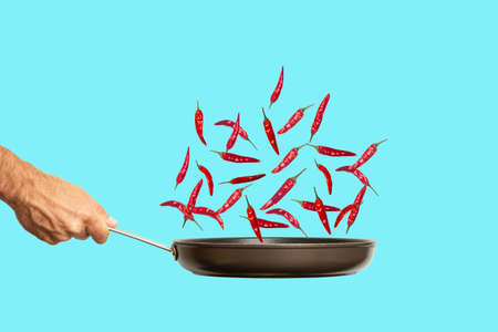 Hand with a frying pan and hot chili pepper on a colored blue background. Food collage, minimal art creative concept. high quality photoの写真素材